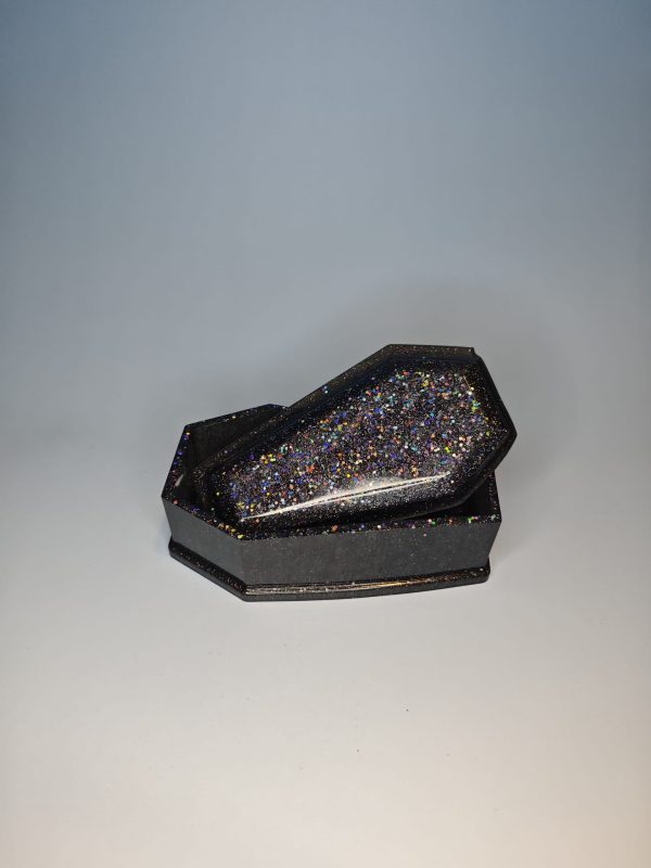 A coffin shaped black box with glittery surface with a lid