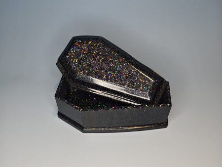 A coffin shaped black box with glittery surface with a lid